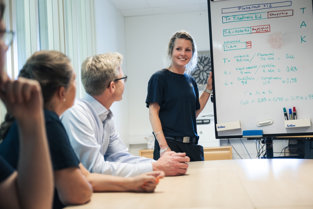 Ett konferensrum med mötesdeltagare, en kvinna vid en white board.